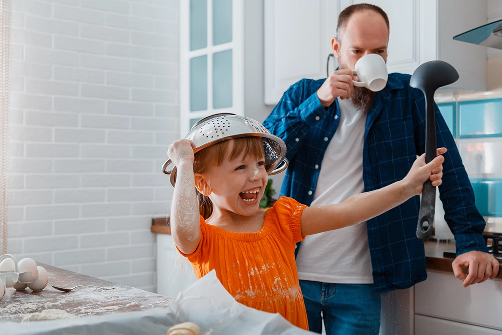 A parent sipping their coffee while watching a child play with kitchen utensils