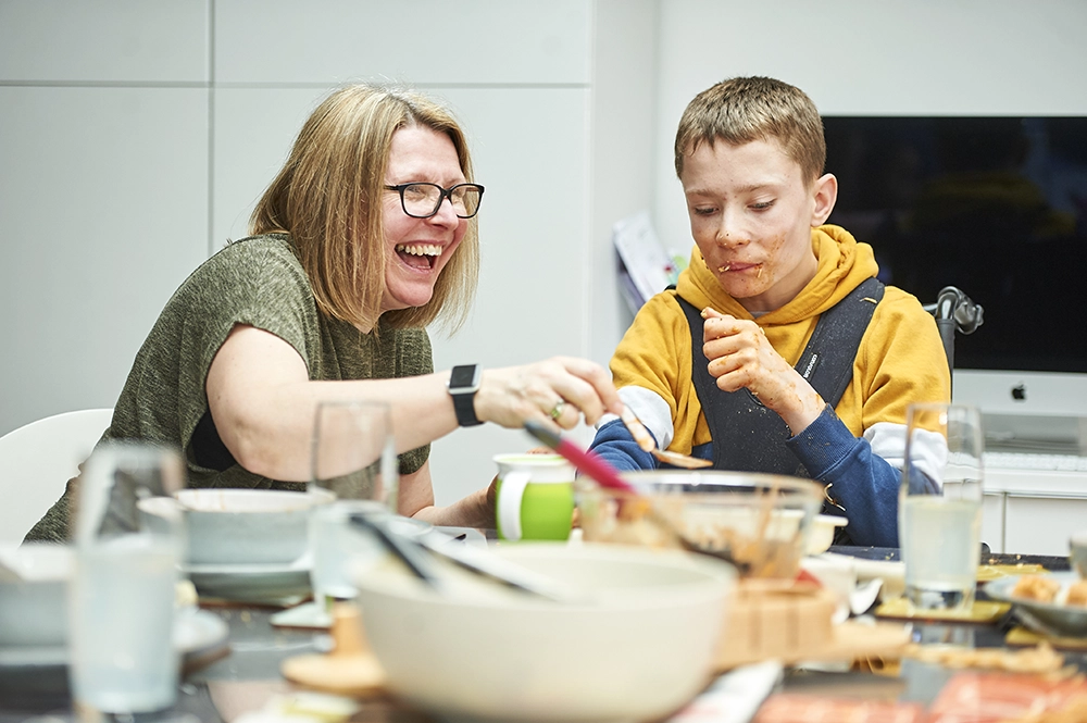 A teenager in an assistive chair having dinner with his mum