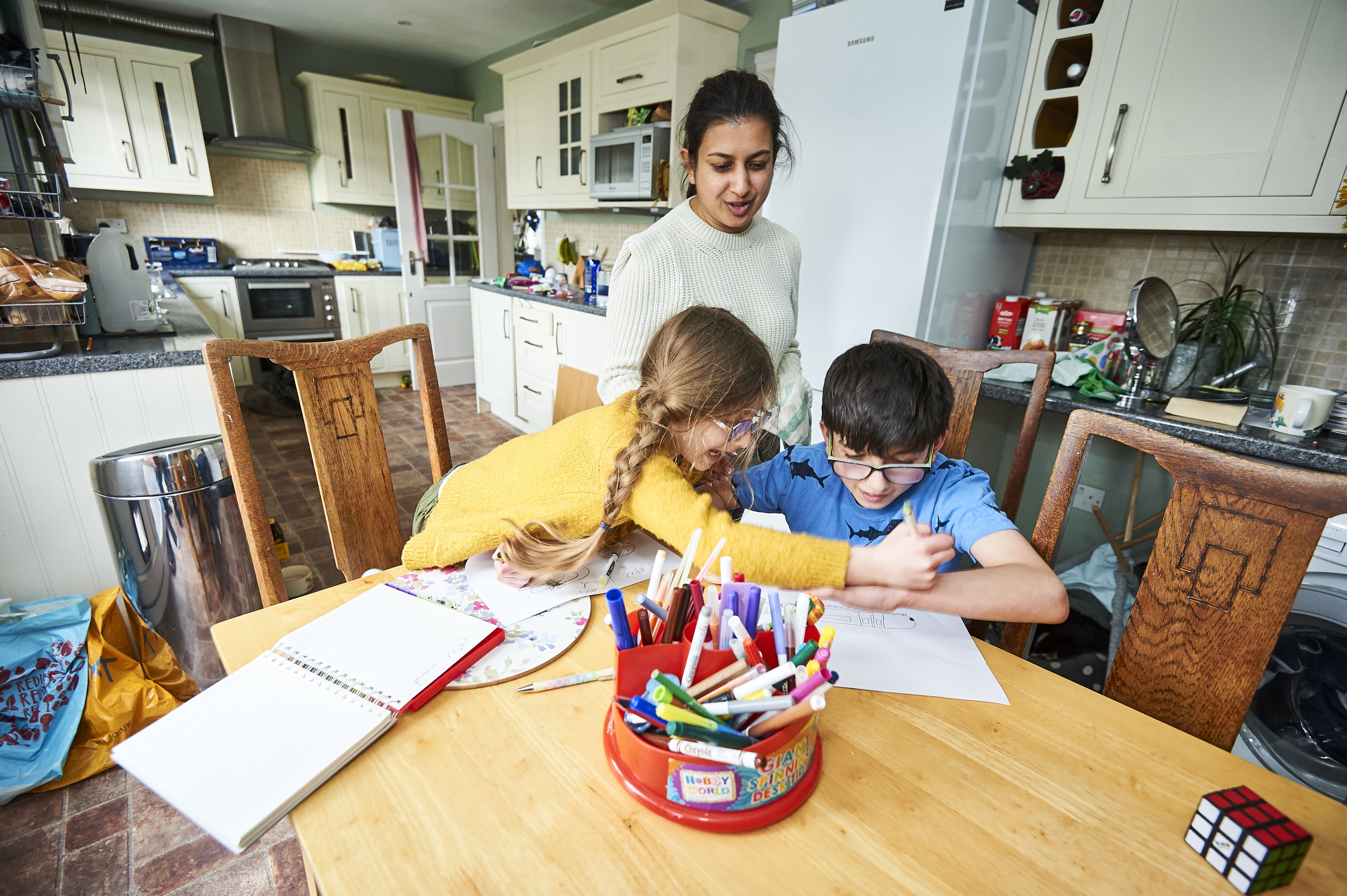 Two children colouring in at the table while their parent looks on